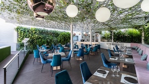 Un restaurante al aire libre con sillas y mesas azules, una zona de bar y vegetación.
