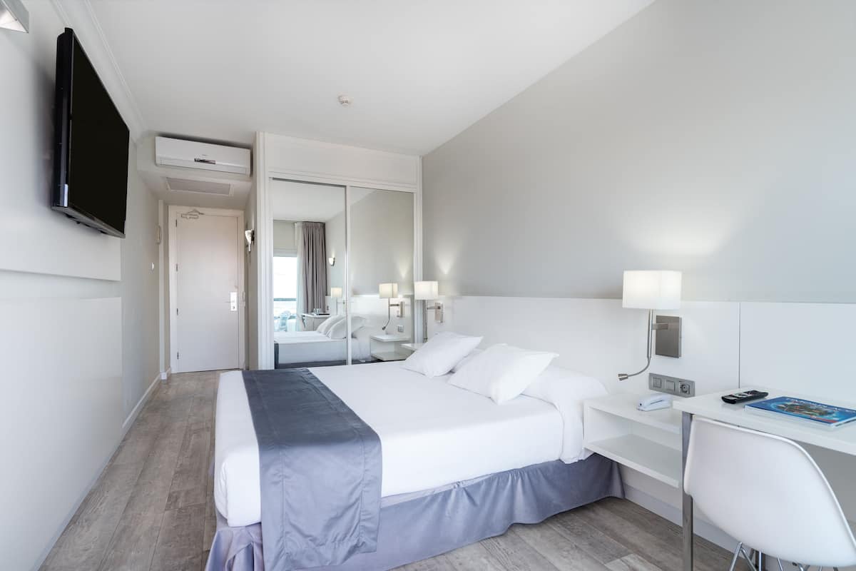 A modern hotel room with a large bed, a desk with a chair, a flat-screen TV, and a mirror.
