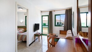 A hotel room with a bed, a TV, a dining table, and a view of the outside. - Apartamentos Las Faluas (San Bartolomé de Tirajana)