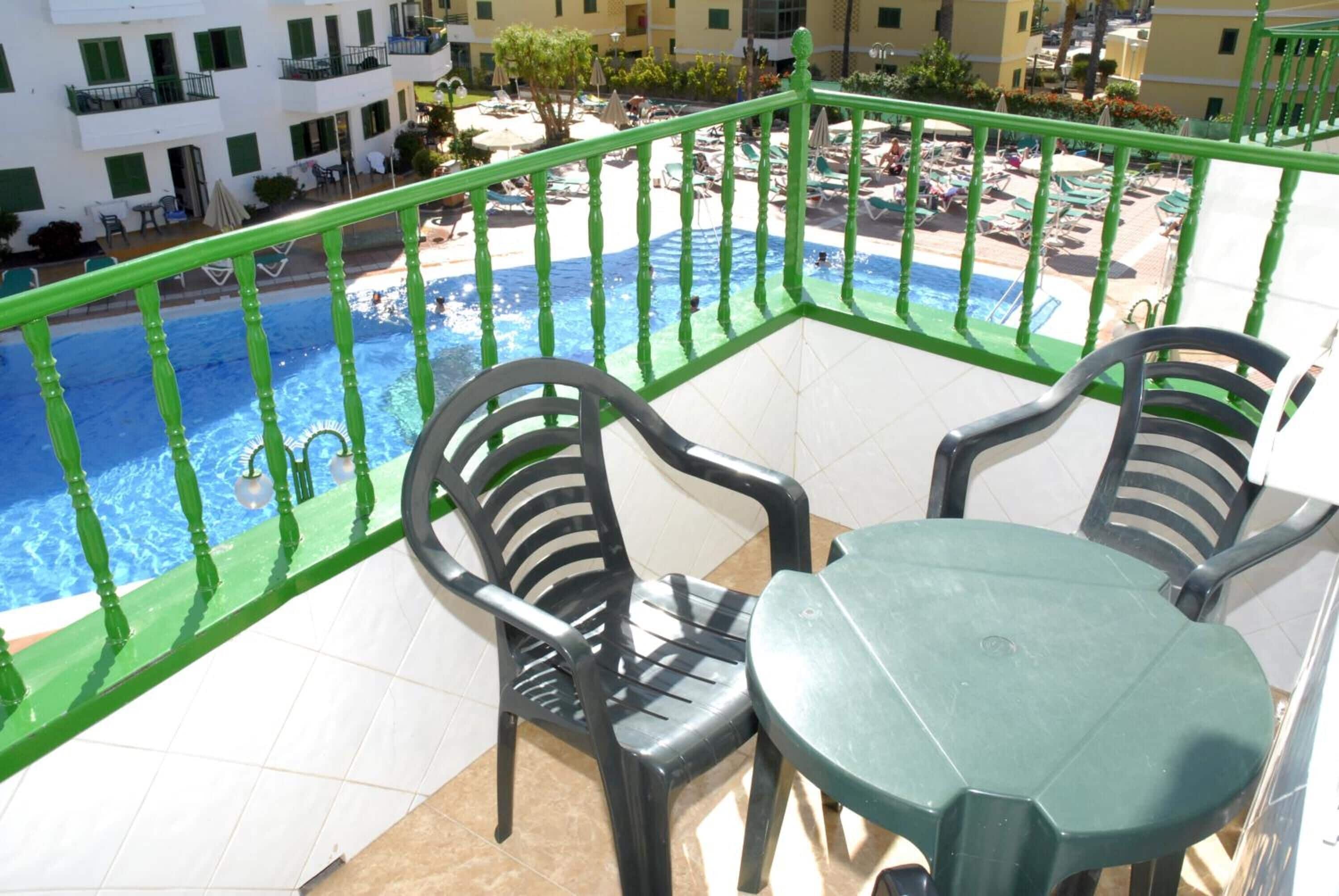 A balcony with a pool view, two chairs, and a table.