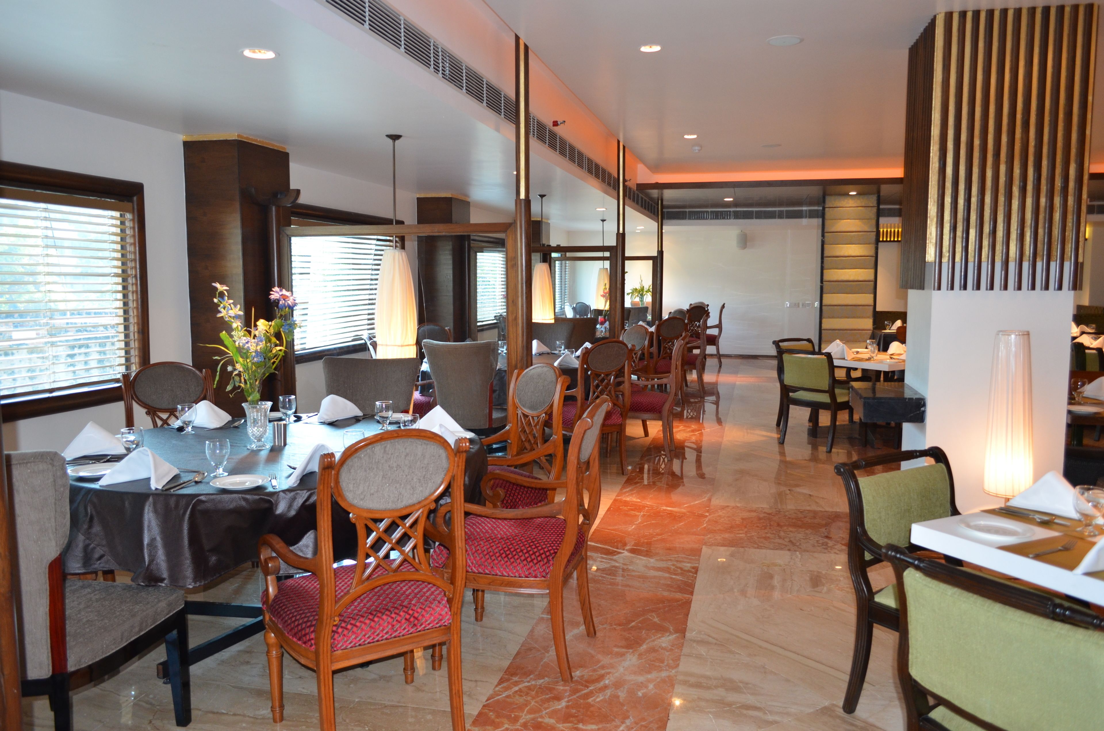 A dining area with tables set for service, wooden chairs, and a large vase with flowers.