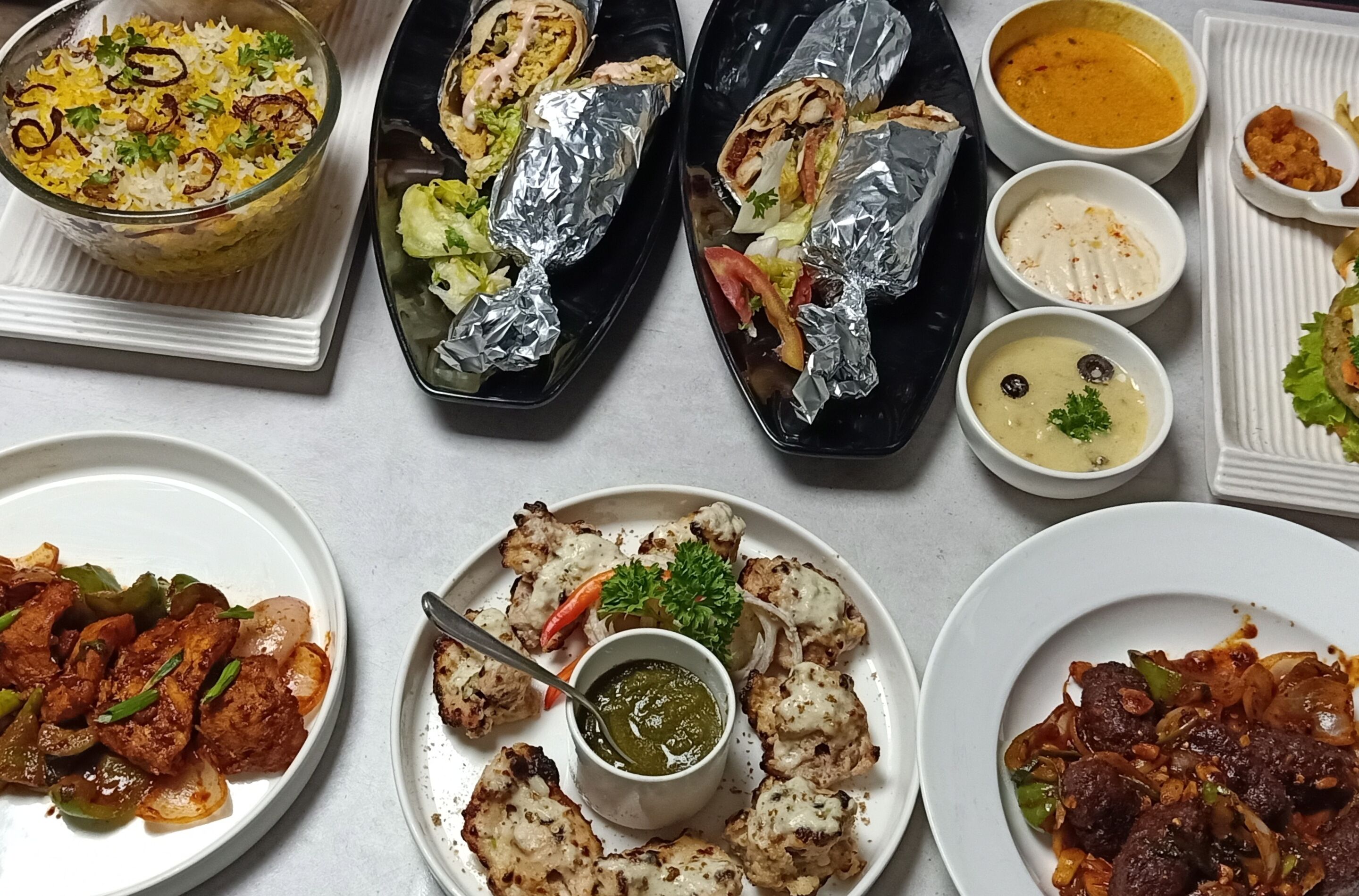 Une variété de plats, notamment du biryani, des wraps et des plats de viande, servis dans plusieurs assiettes et bols.