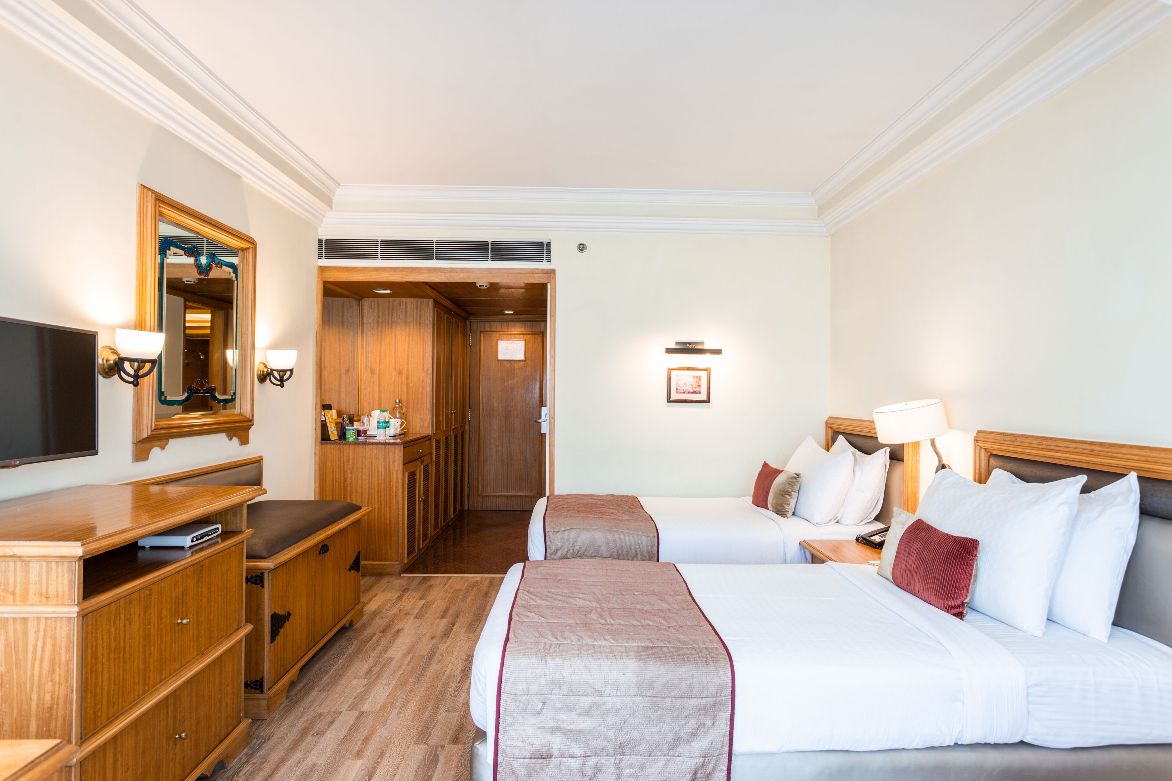 Une chambre d’hôtel avec deux lits, une télévision, des meubles en bois et un miroir.