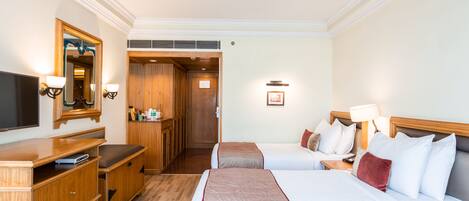 Une chambre d’hôtel avec deux lits, une télévision, des meubles en bois et un miroir.