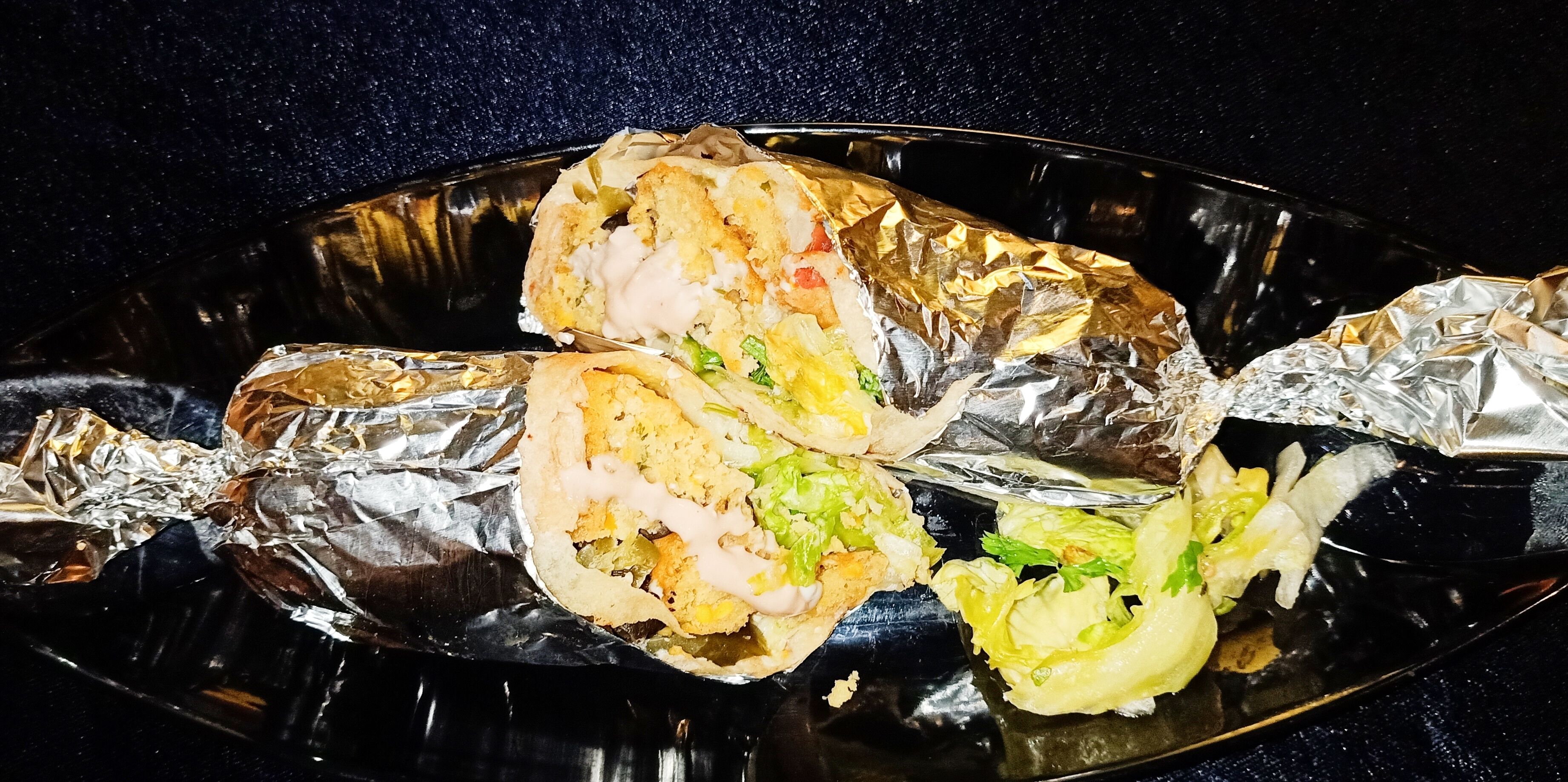 Pescado envuelto en papel de aluminio sobre un plato negro.