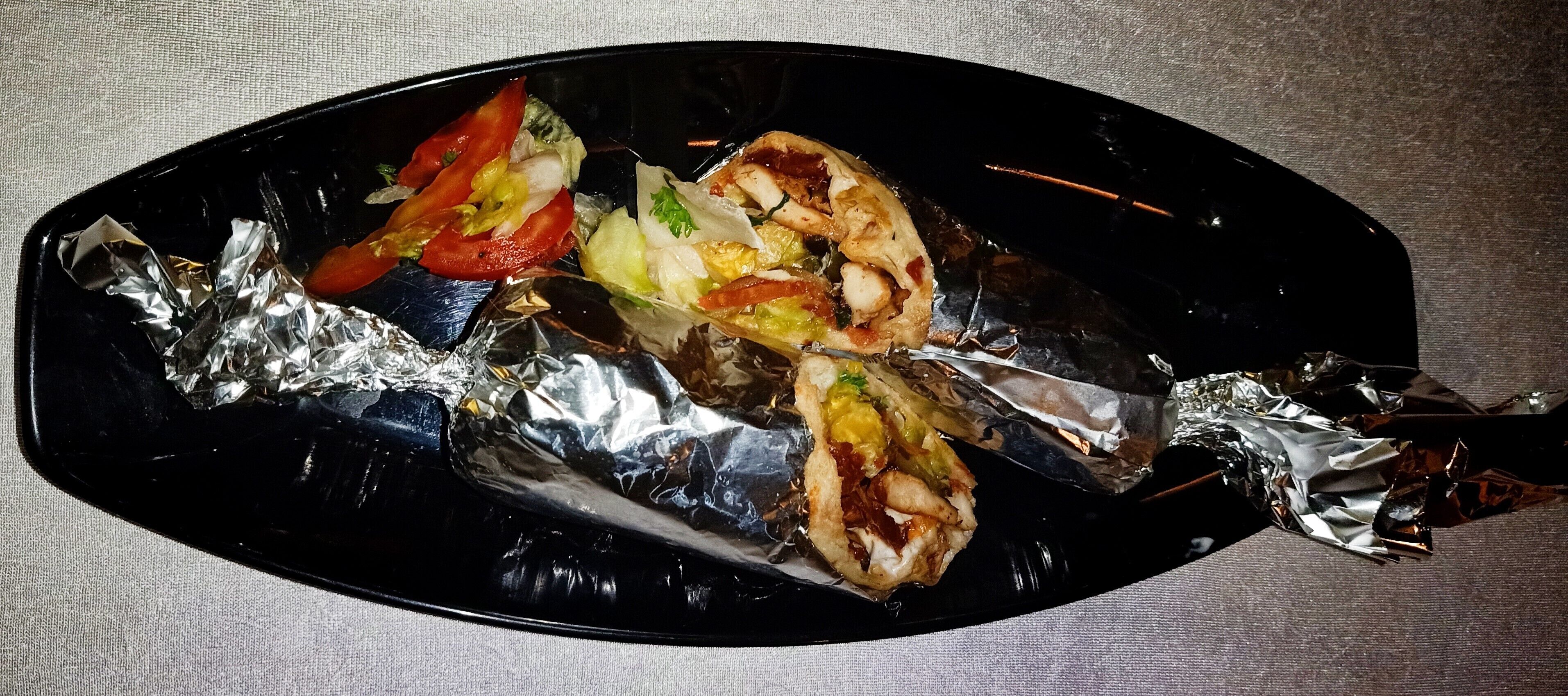 A black oval plate with a grilled fish fillet, vegetables, and condiments.