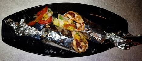 A black oval plate with a grilled fish fillet, vegetables, and condiments.