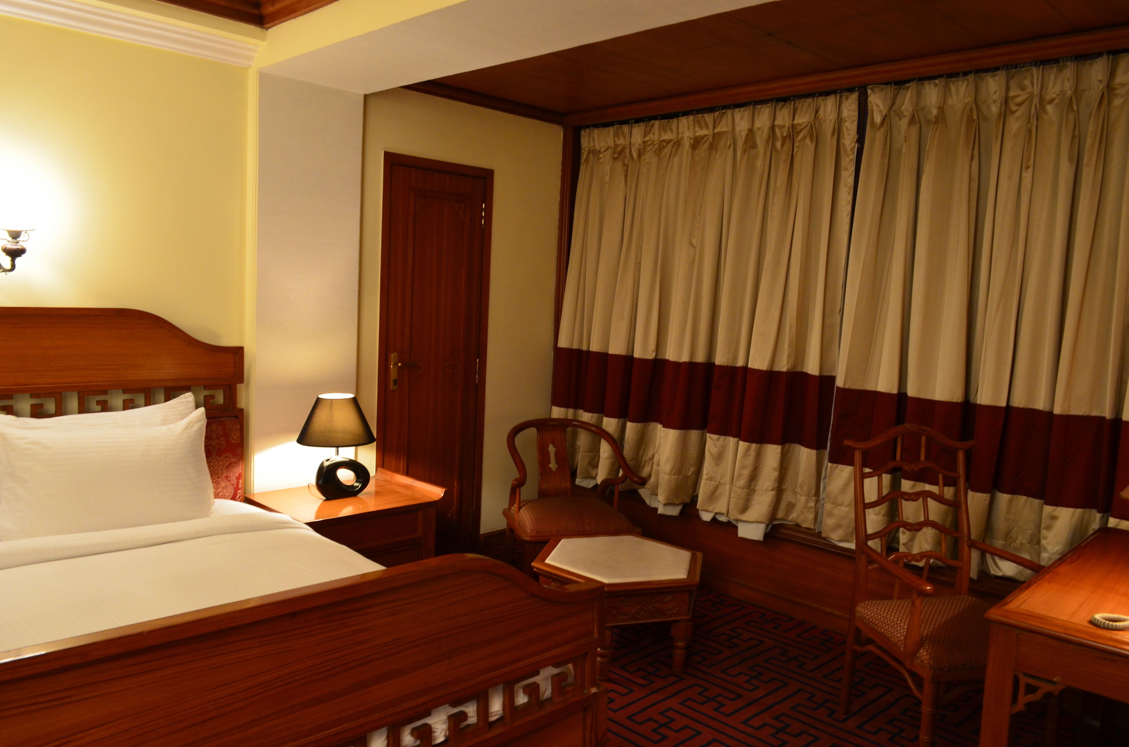 Ein Hotelzimmer mit einem Holzbett, einem Schreibtisch, einem Stuhl und einem Fenster mit Vorhängen.
