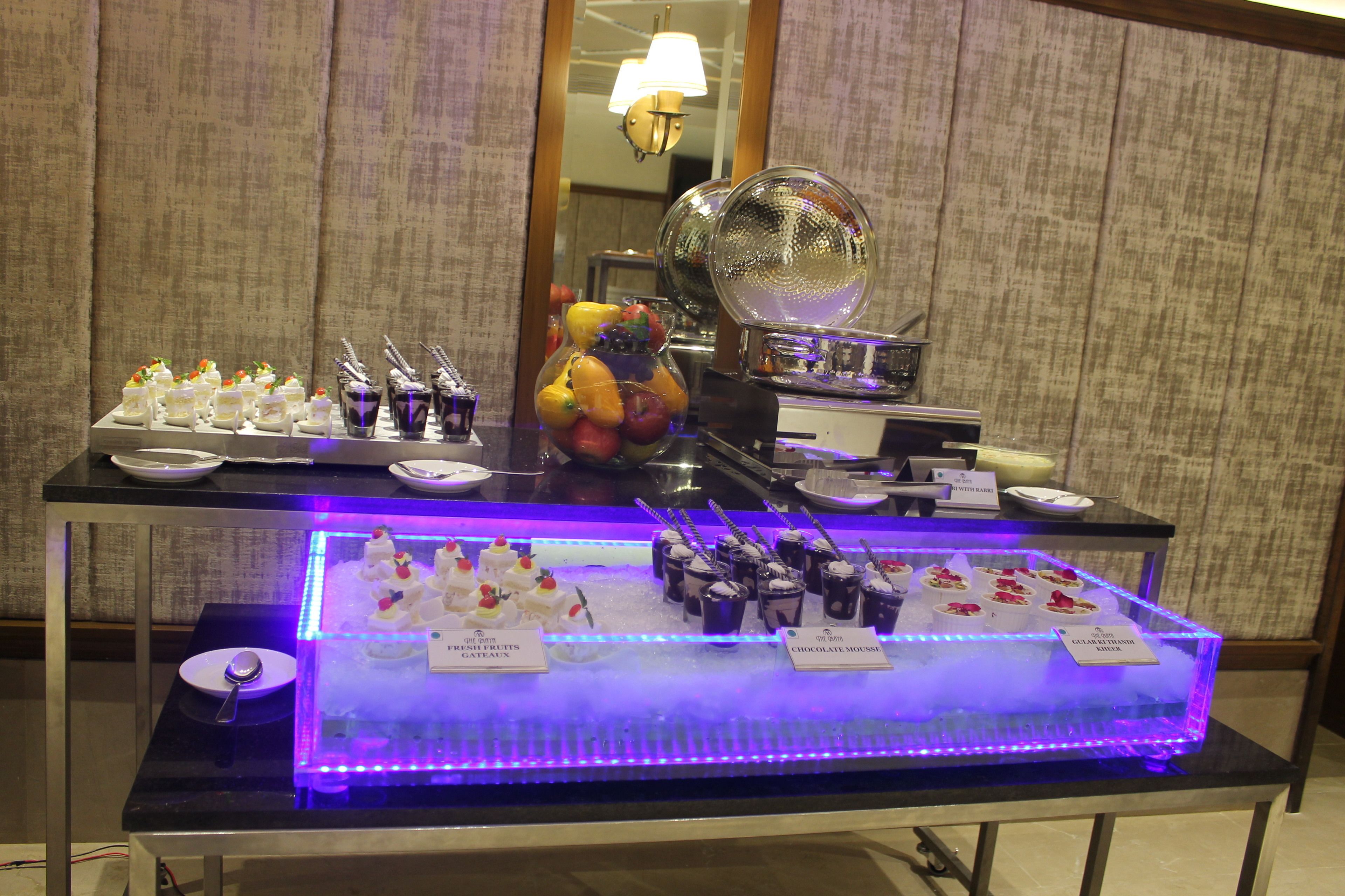 A buffet table with various desserts and a glass display case with a blue light.