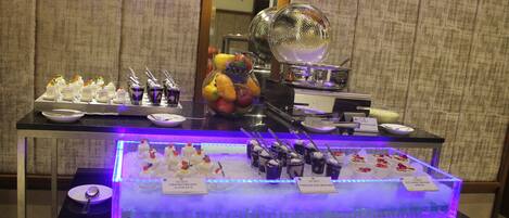Uma mesa de buffet com diversos doces e um expositor de vidro com luz azul.