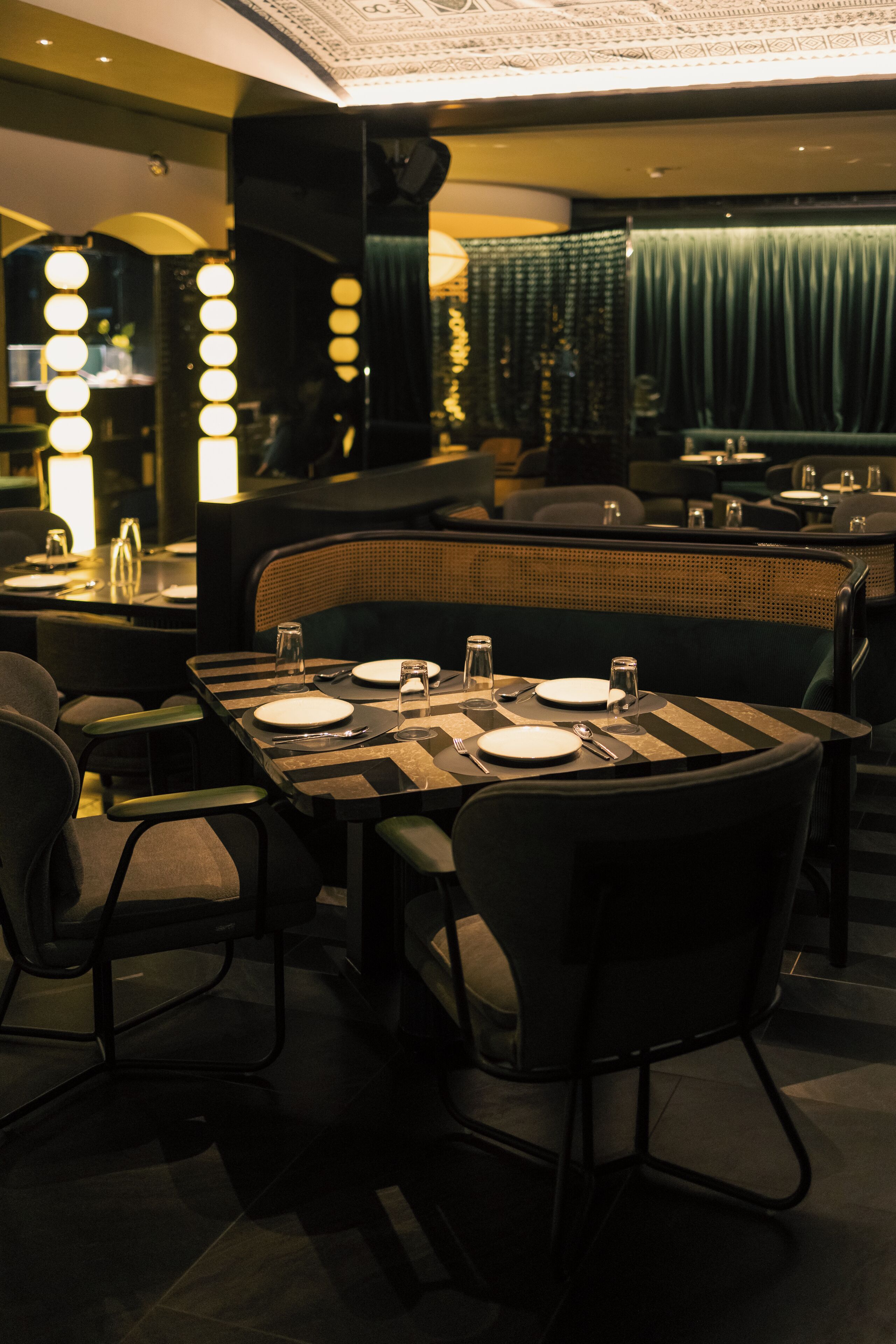 A restaurant with a dark interior, striped tablecloths, and a green curtain backdrop.