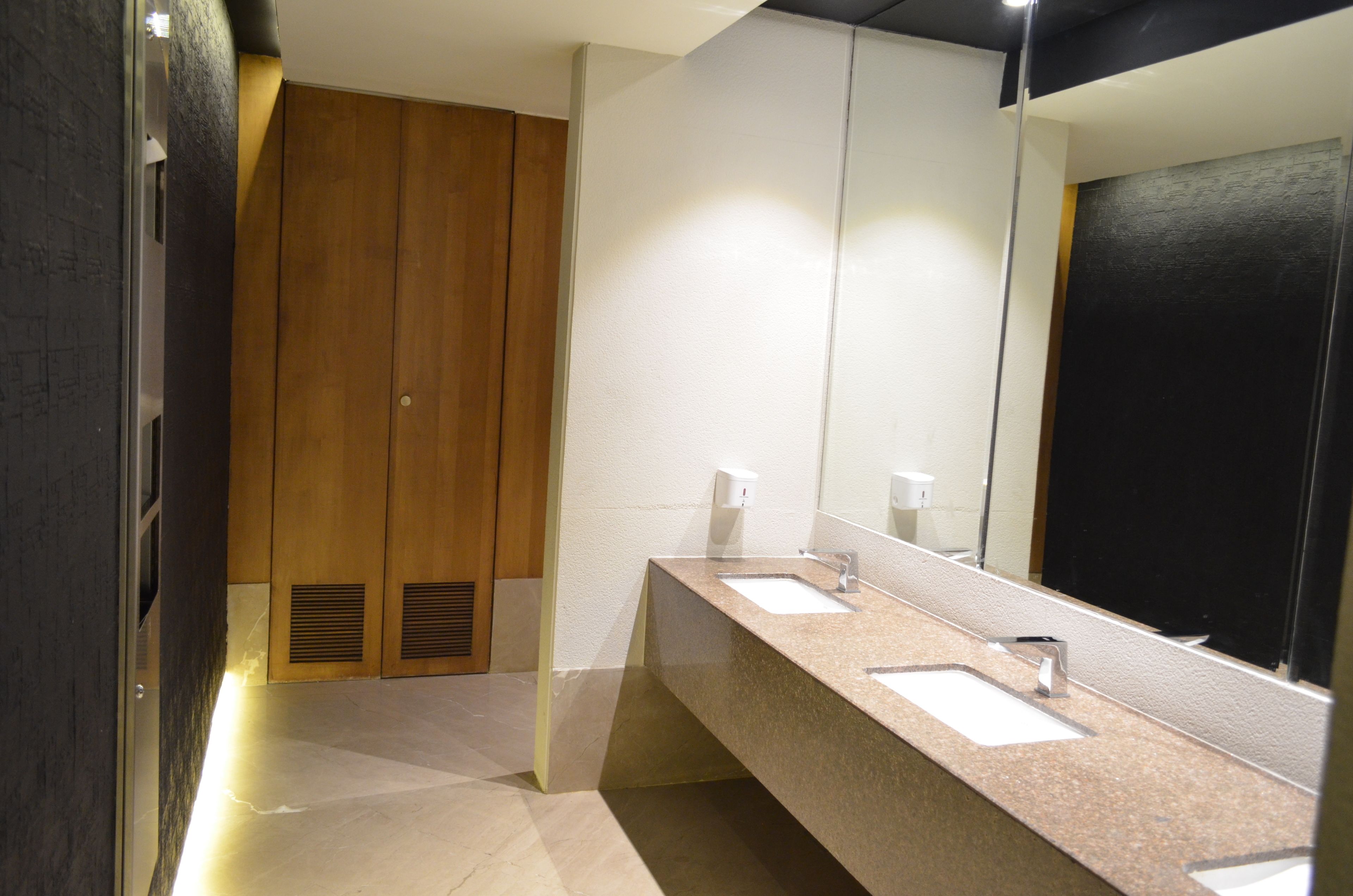 Un baño moderno con dos lavamanos, un espejo grande y taquillas de madera.