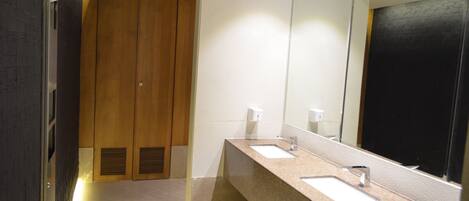 Un baño moderno con dos lavamanos, un espejo grande y taquillas de madera.