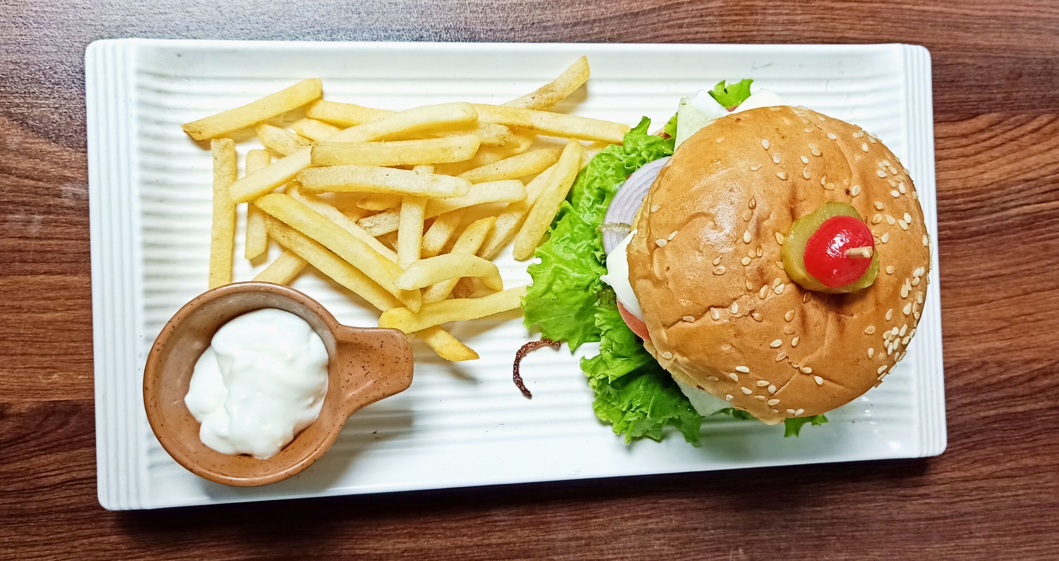 A plate with a burger, French fries, and a small bowl of sauce.