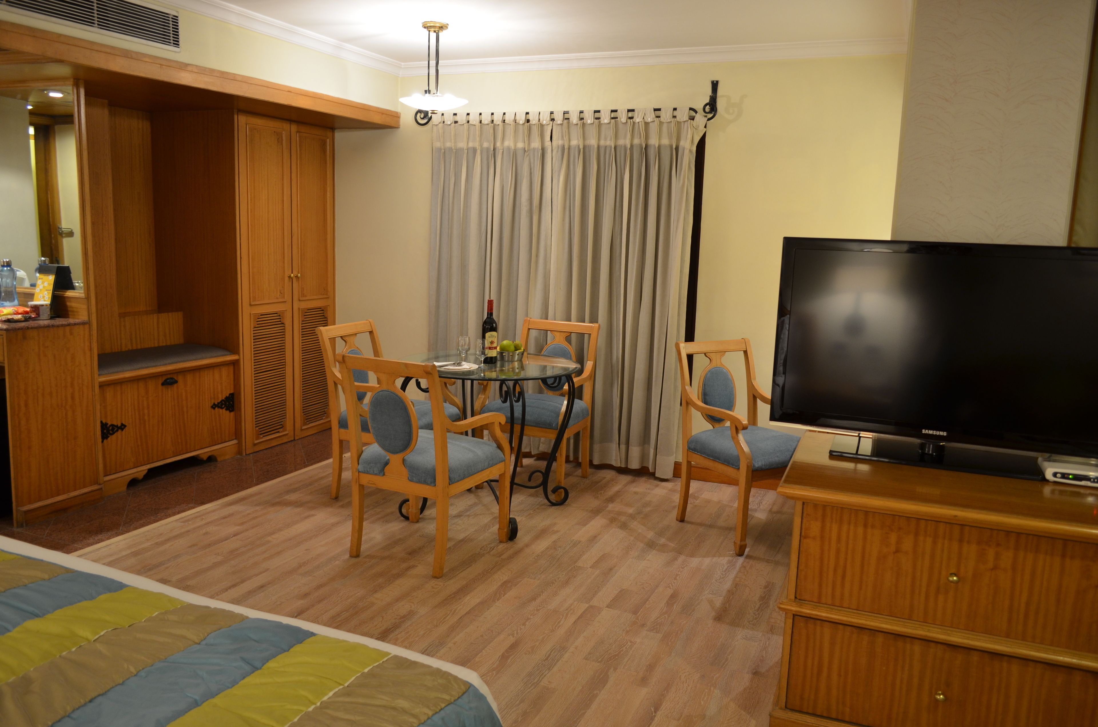 Habitación de hotel con cama, televisión, mesa de comedor con sillas, armario y cortina.