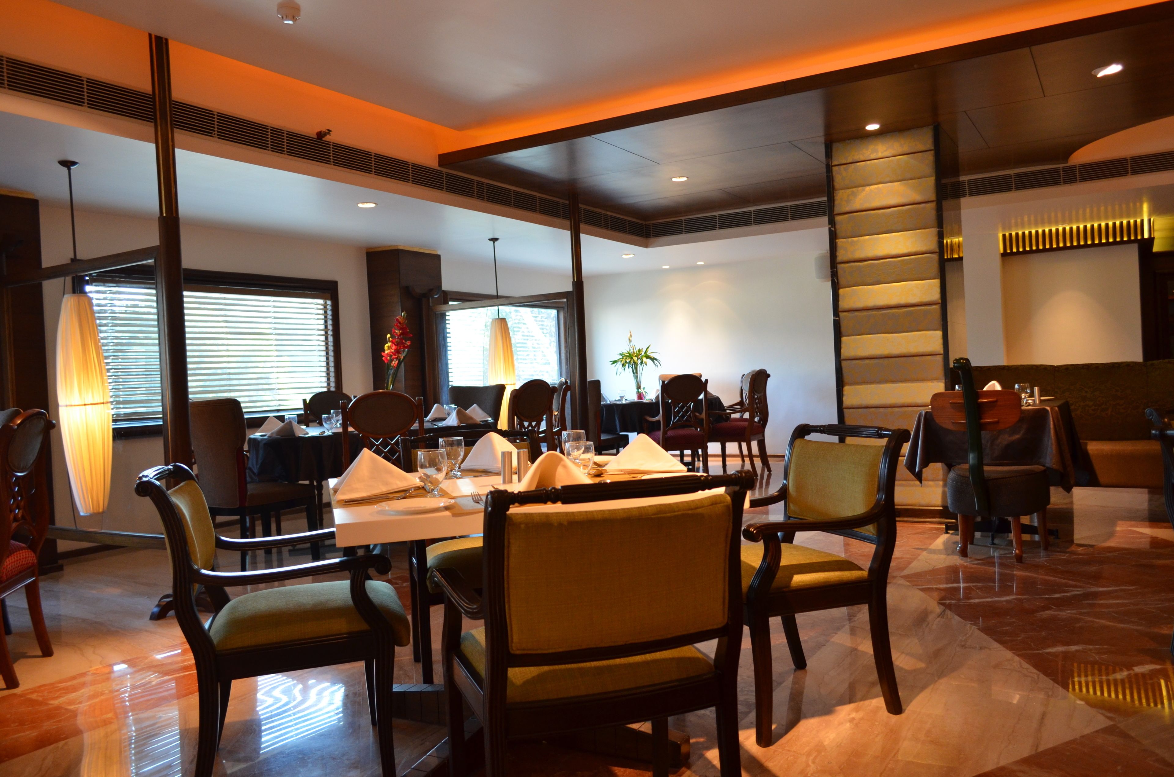 Un restaurante con varias mesas y sillas, amplias ventanas con persianas y una decoración interior moderna.
