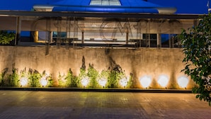 Un hotel moderno con un cartel llamativo en la parte superior, una entrada cubierta y un camino bien iluminado con plantas.