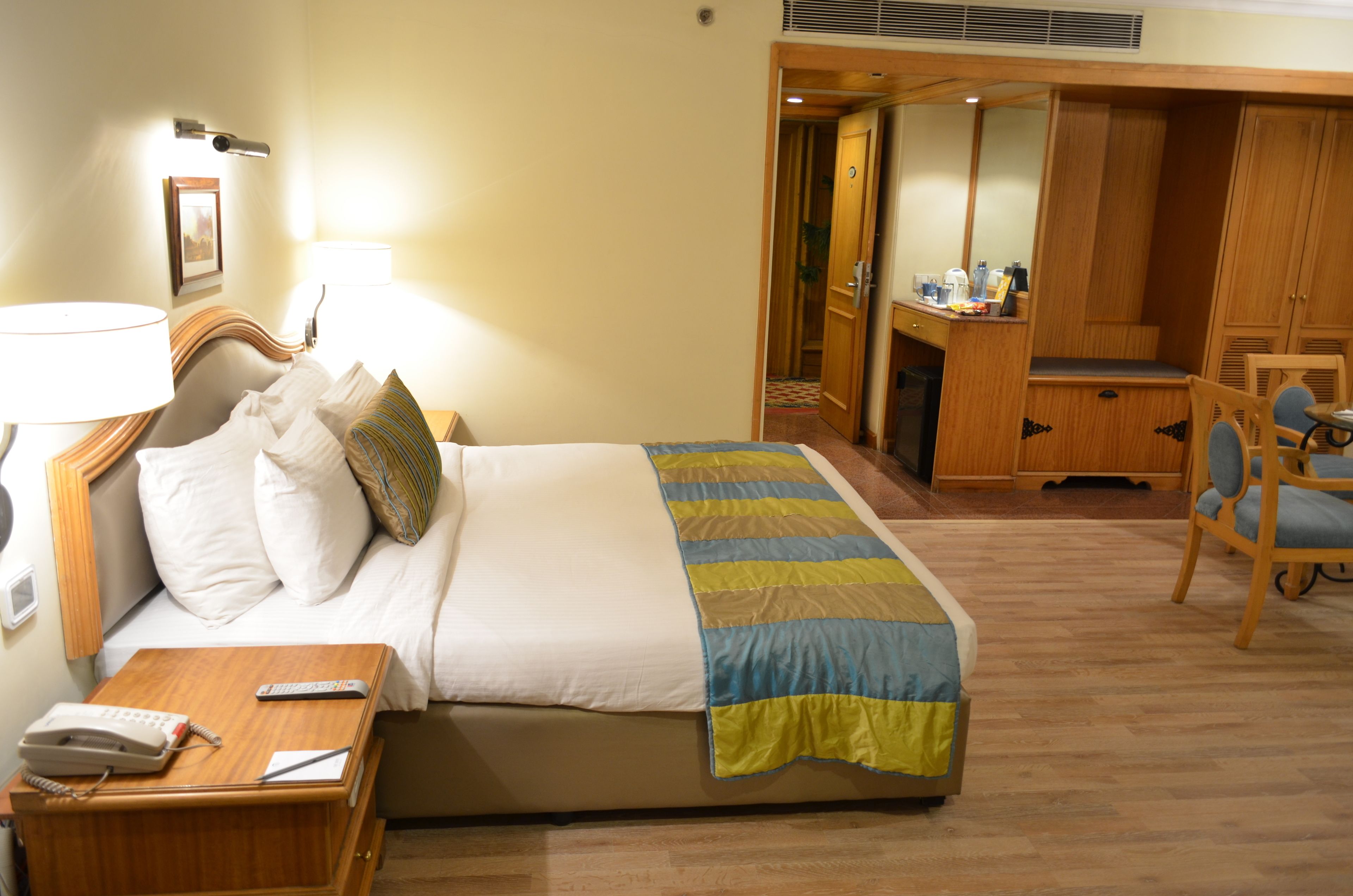 A hotel room with a bed, bedside table, lamp, and a desk with a chair.