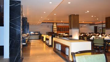 A modern hotel lobby with marble columns, a reception desk, and a dining area with tables and chairs.