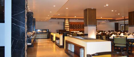 A modern hotel lobby with marble columns, a reception desk, and a dining area with tables and chairs.