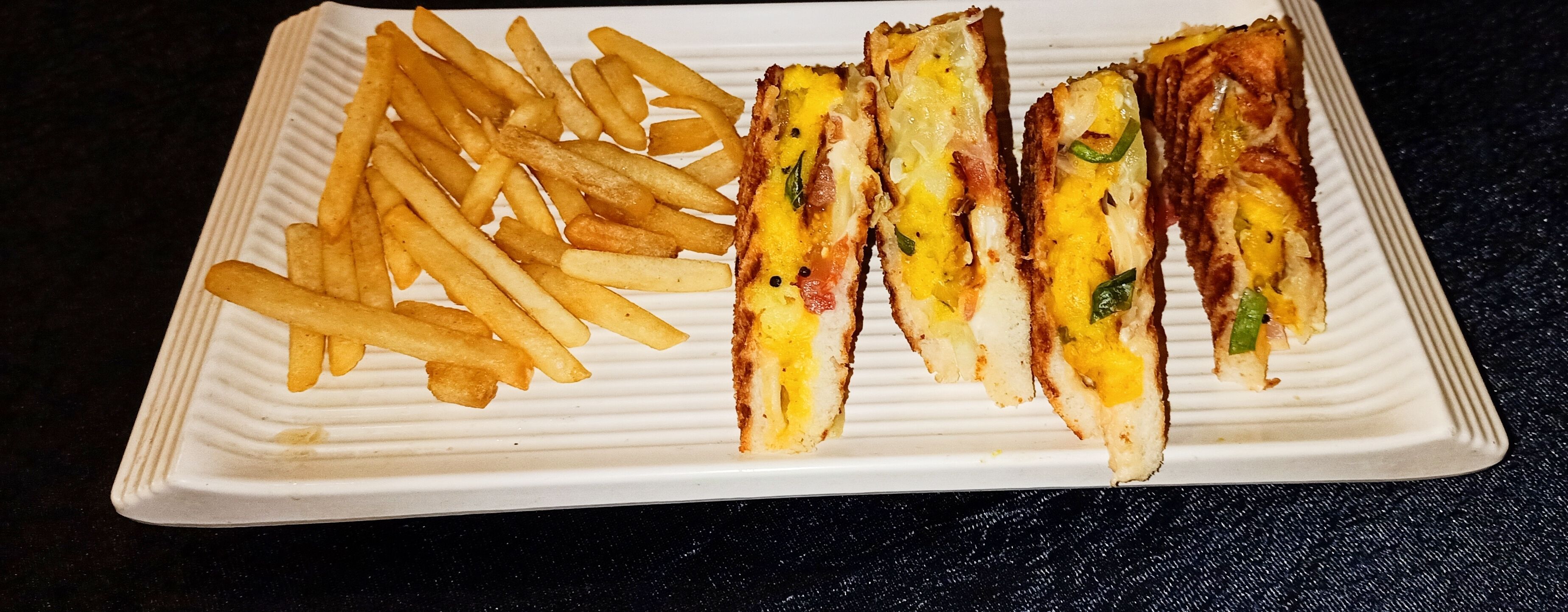 A white rectangular plate with French fries and grilled sandwiches.