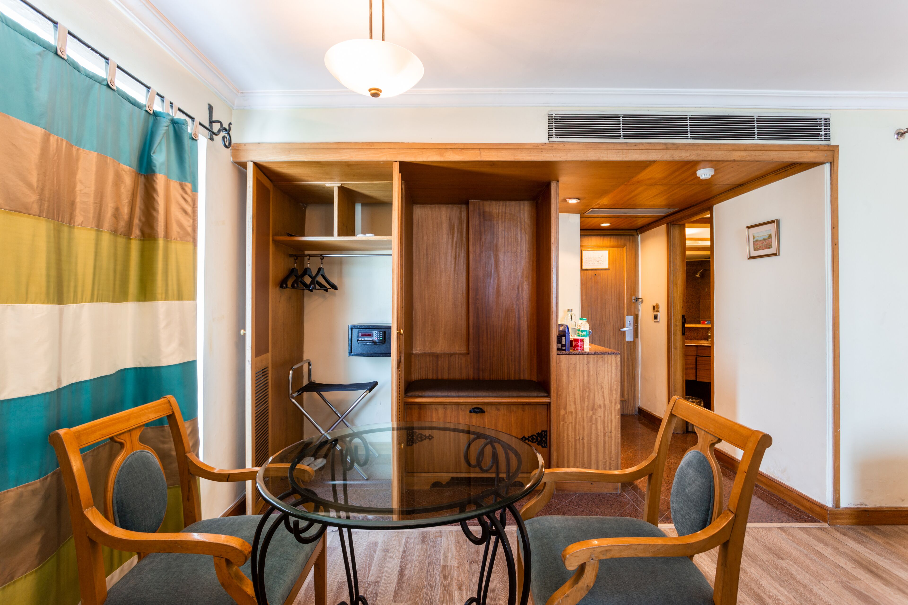 Een kamer met een glazen tafel, twee houten stoelen, een gestreept gordijn en een houten kast.