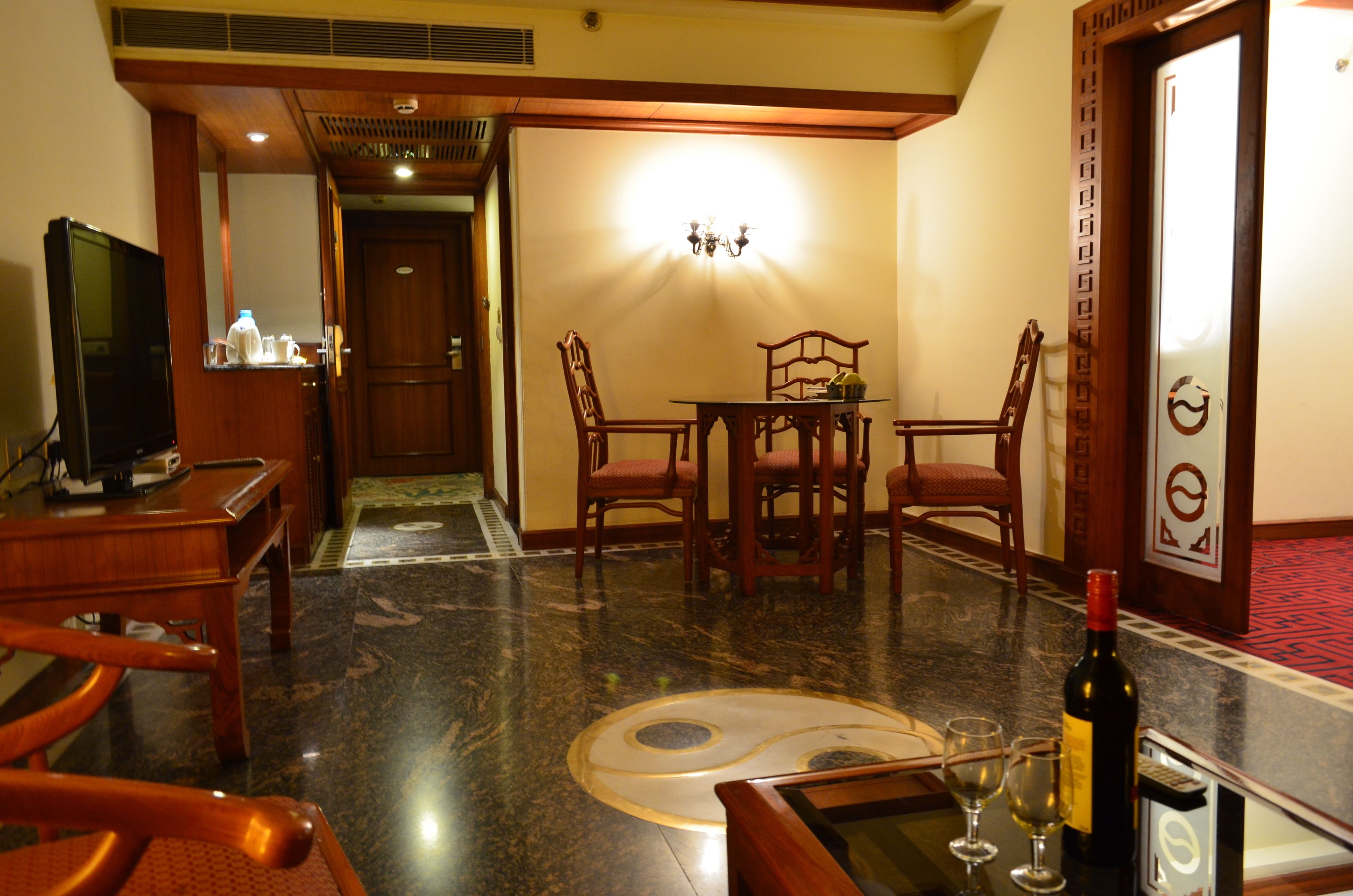 A hotel room with a dining area featuring a wooden table and chairs, a television, and a bottle of wine.
