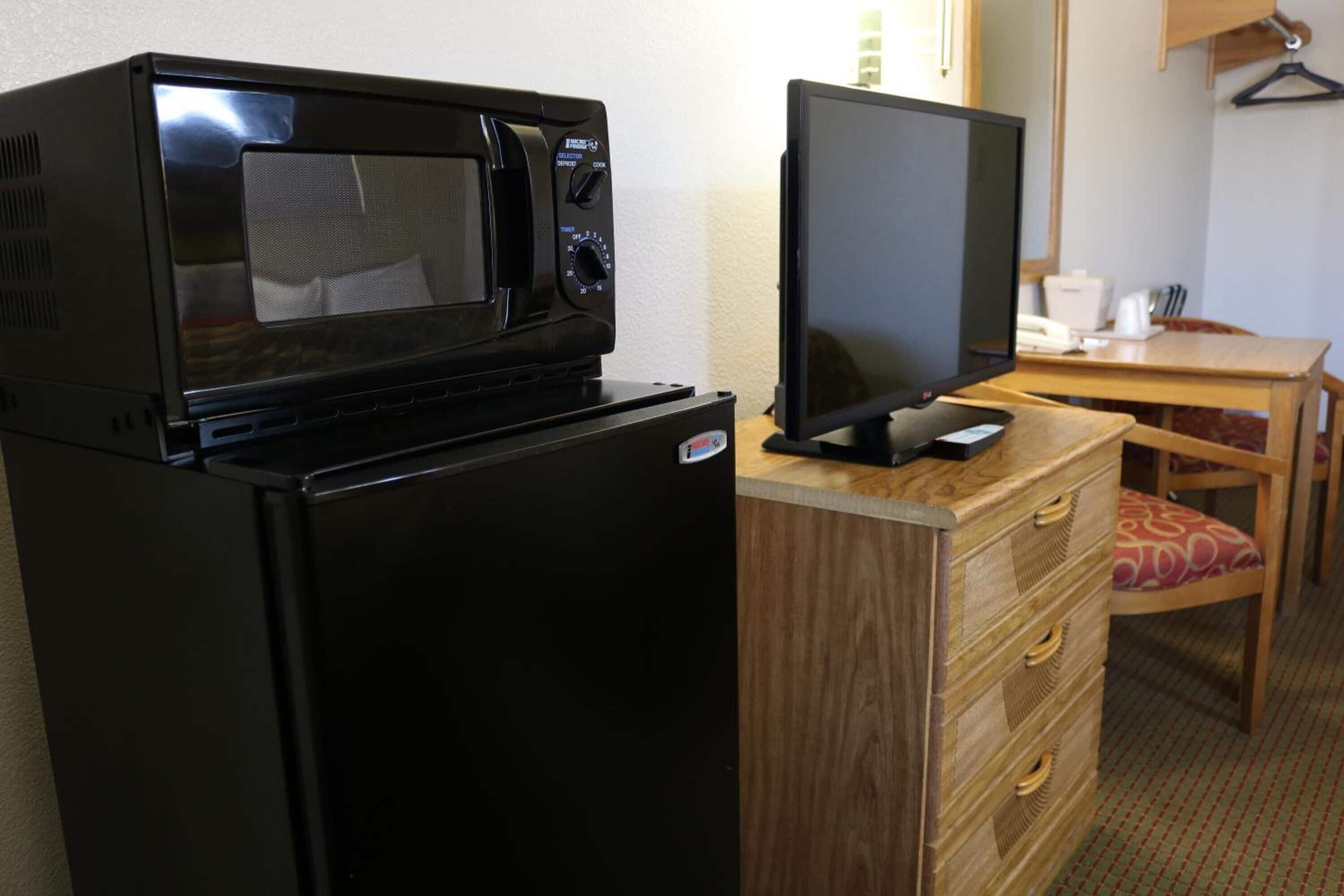 Una kitchenette compacta con microondas y un televisor de pantalla plana sobre un aparador de madera.