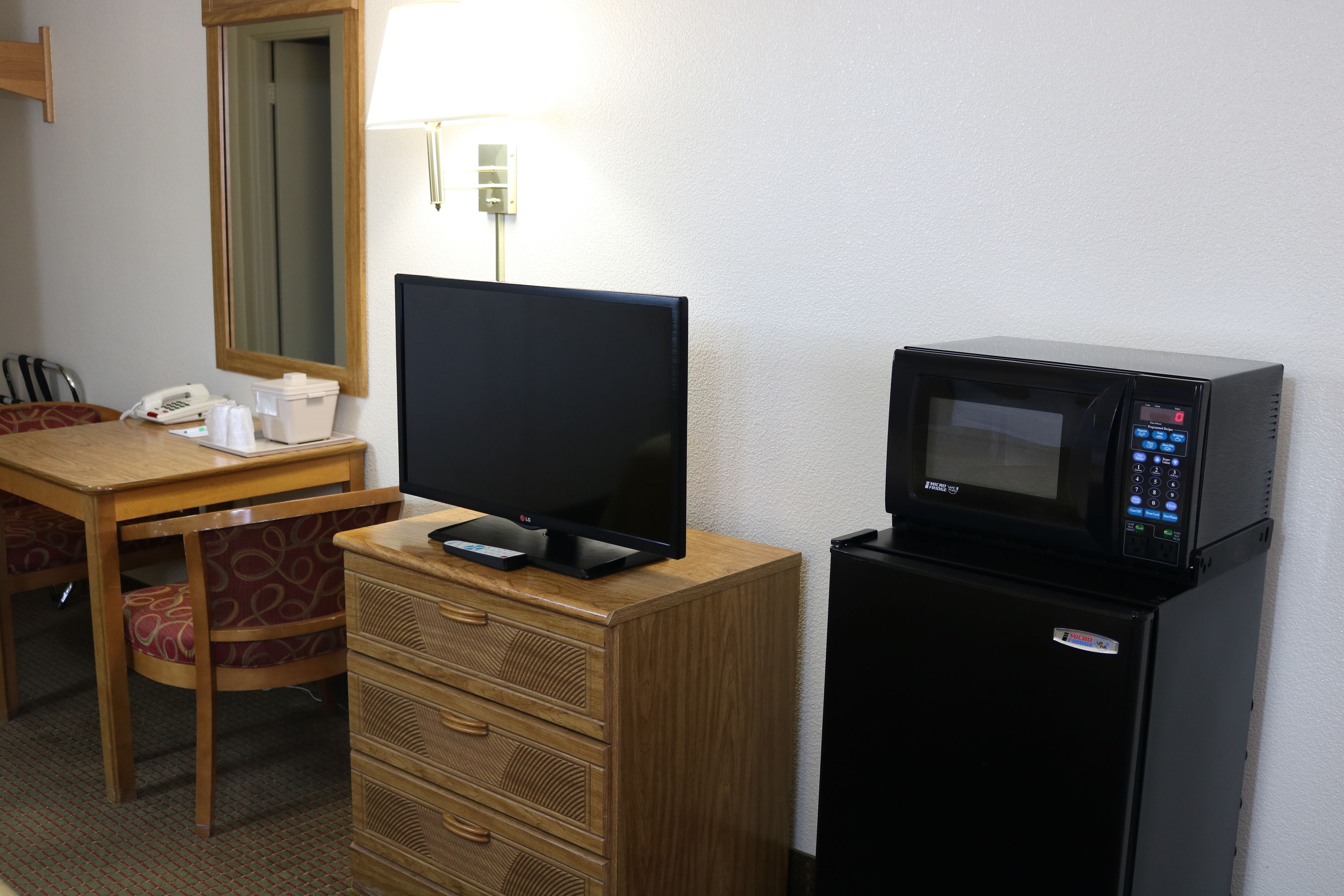 A hotel room with a wooden desk, a television, a microwave, and a refrigerator.
