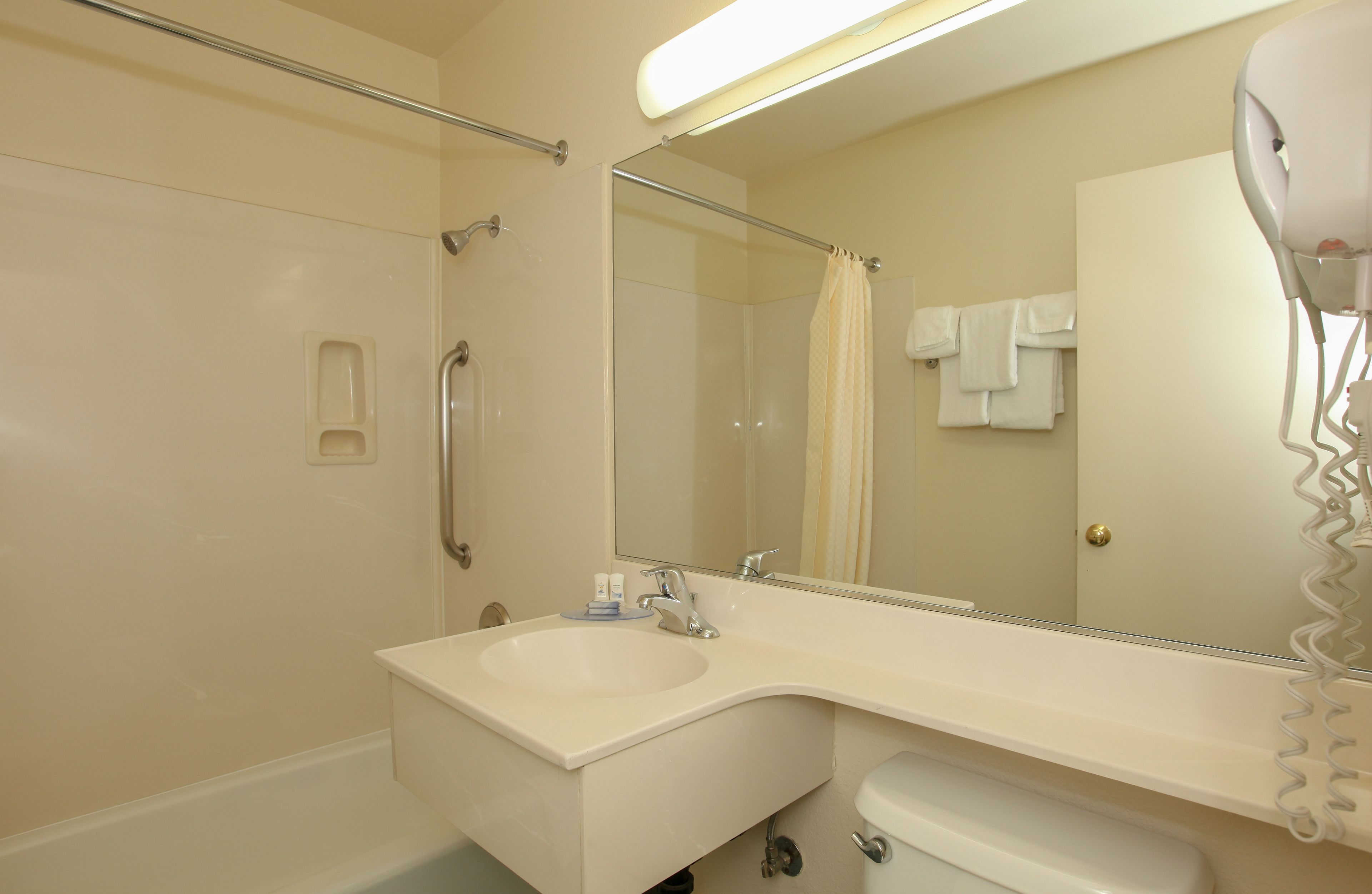 A bathroom with a sink, mirror, shower, and hairdryer.