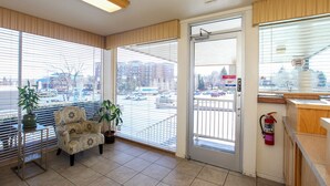 A hotel room with a large window, a chair, a small table with a potted plant, and a fire extinguisher on the wall. - Highland Country Inn (Flagstaff)