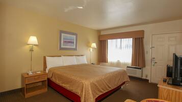 A hotel room with a large bed, two bedside lamps, a flat-screen TV, a desk with a computer, and a window with curtains.