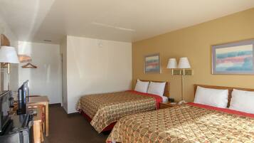A hotel room with two beds, a desk with a television, and a lamp.