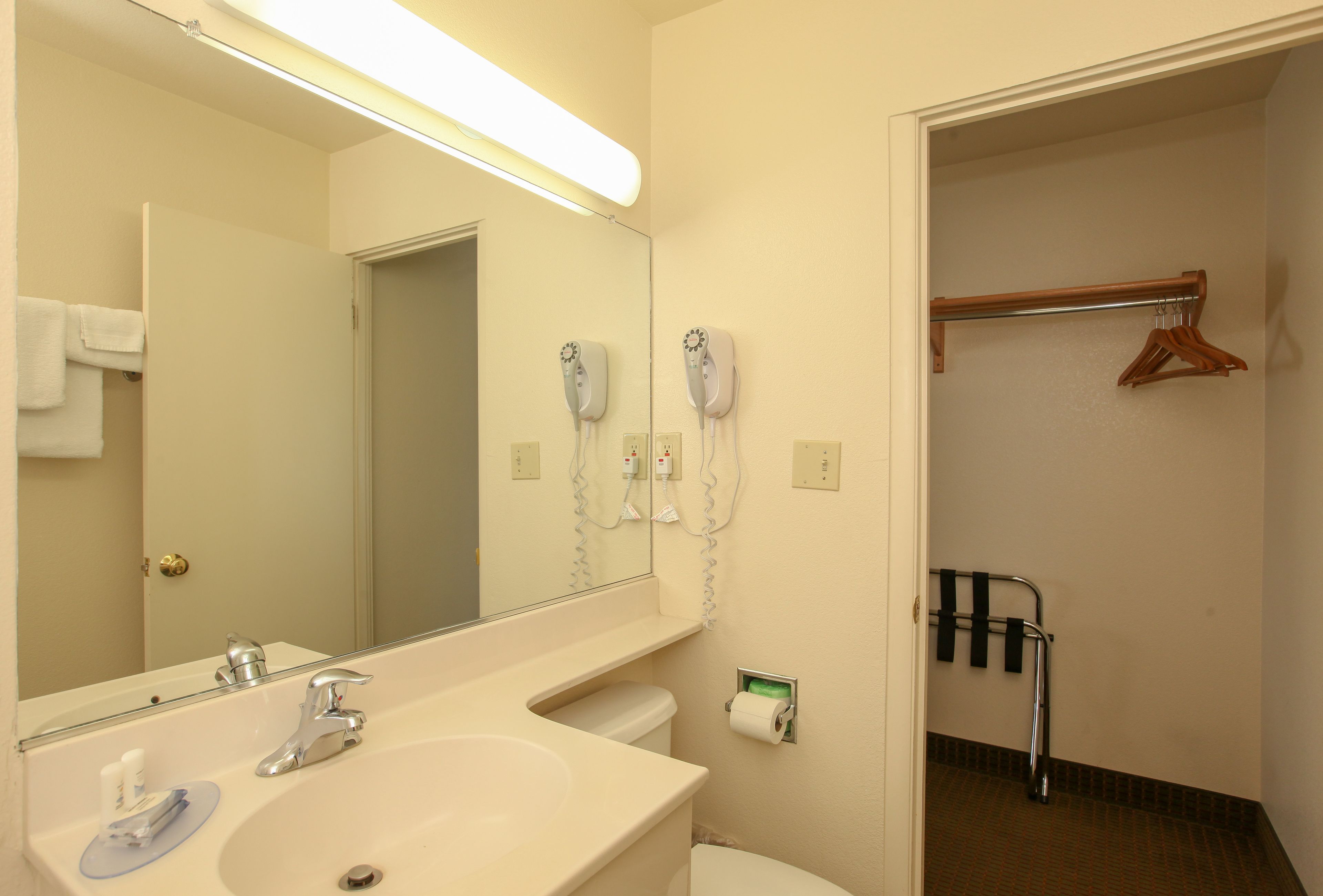 A bathroom with a sink, mirror, hair dryers, and a towel rack.