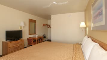 A hotel room with a large bed, a television, a desk with a chair, a mirror, and a wall-mounted lamp.