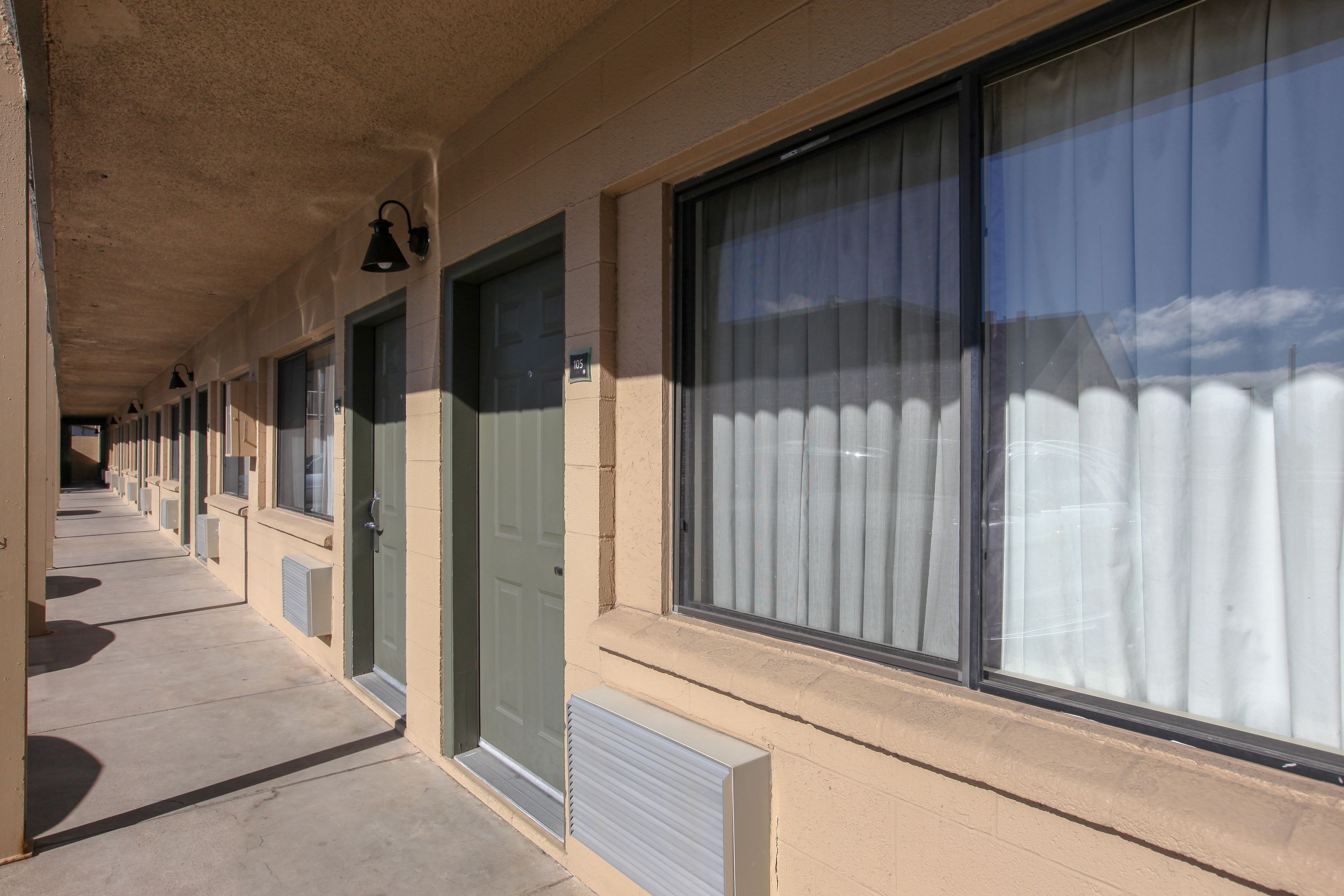 A row of hotel rooms with large windows, air conditioning units, and a concrete corridor.