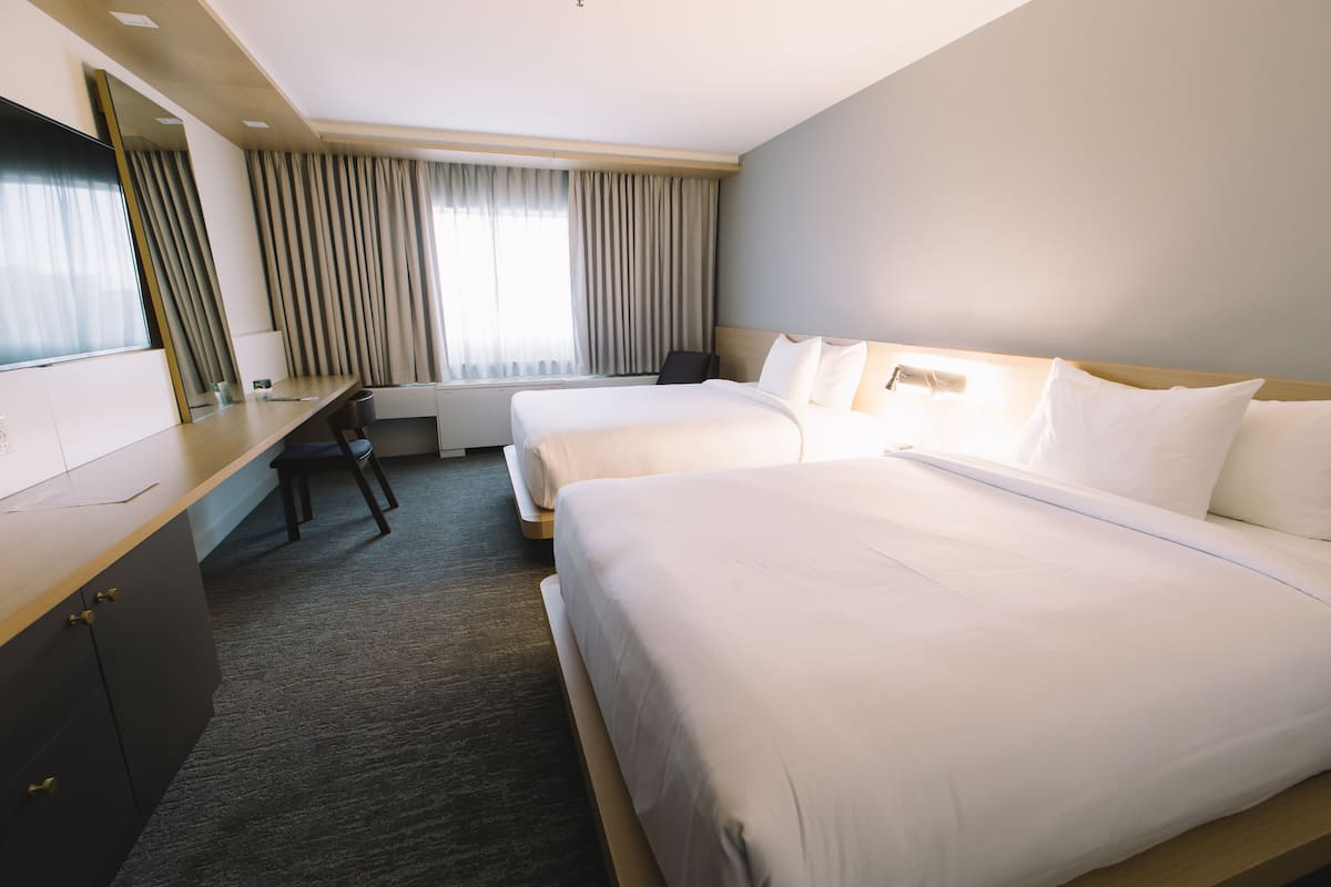 A hotel room with two beds, a desk, a chair, a TV, and a window with curtains.
