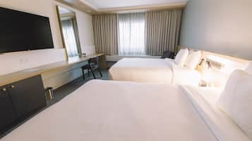 A hotel room with two beds, a desk, a chair, a TV, and a large window with curtains.