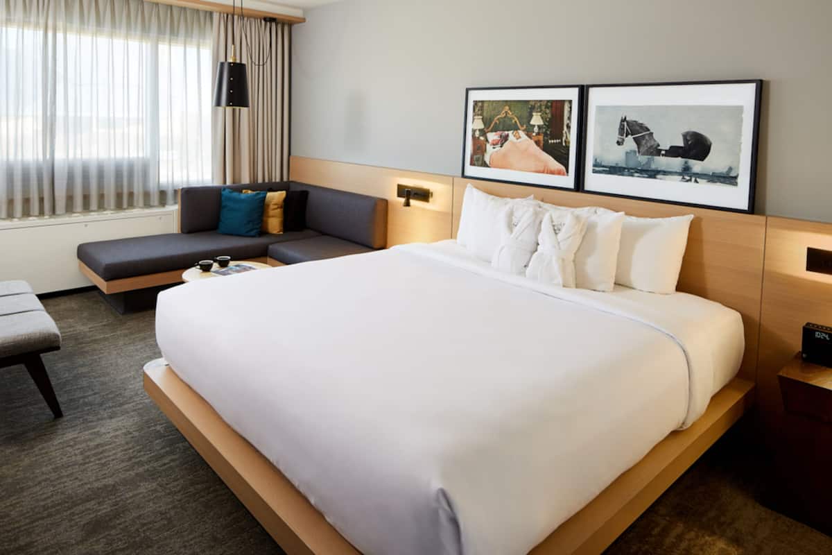 A hotel room with a large bed, a sofa, a desk, and a window with curtains.