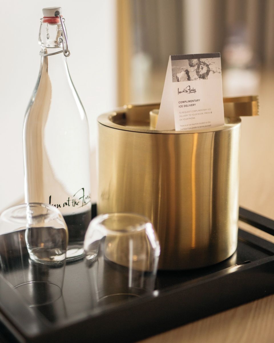Una bandeja con una botella de vidrio, un recipiente dorado y una tarjeta con texto.