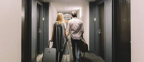 Un passadís amb parets fosques i portes, una làmpada al sostre i una maleta a terra.