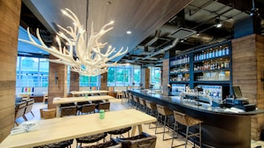 Un área de bar moderna con una isla central, asientos y una lámpara de araña grande.