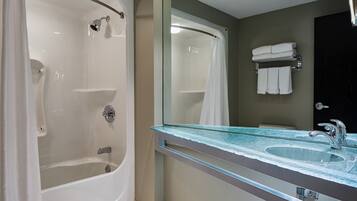 A bathroom with a glass-enclosed bathtub, a sink with a glass countertop, and a towel rack with folded towels.