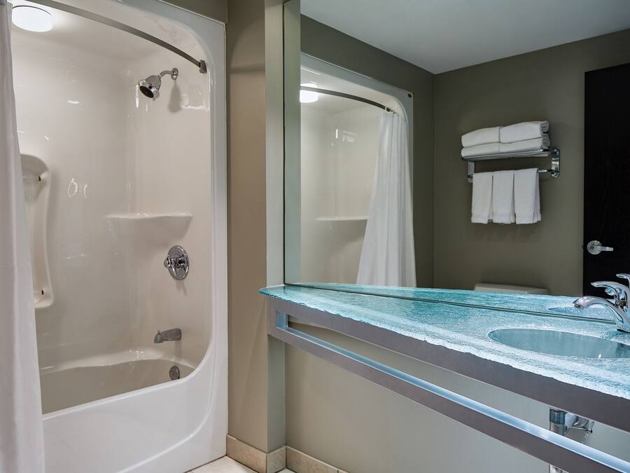 A bathroom with a glass-enclosed bathtub, a sink with a glass countertop, and a towel rack with folded towels.