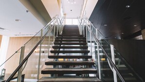 Un interior moderno con una escalera que sube, barandillas de vidrio y un alto techo con iluminación empotrada.