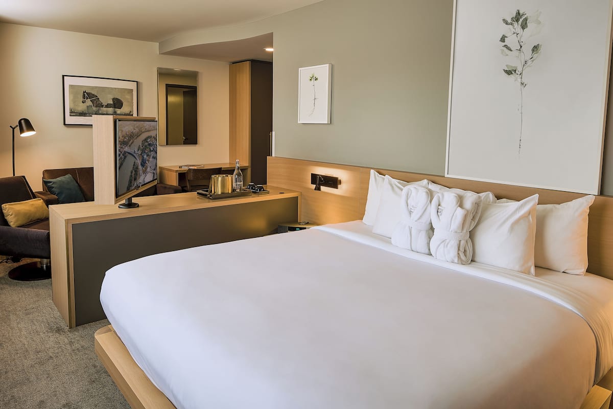 A modern hotel room with a large bed, a desk, a chair, and a flat-screen TV.