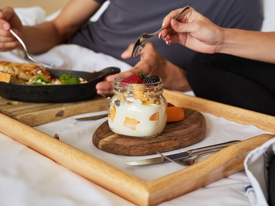 A breakfast tray with a skillet, a jar of yogurt with fruits, and a piece of toast.