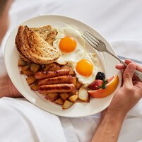 A plate of breakfast food including eggs, toast, sausages, and fruit.