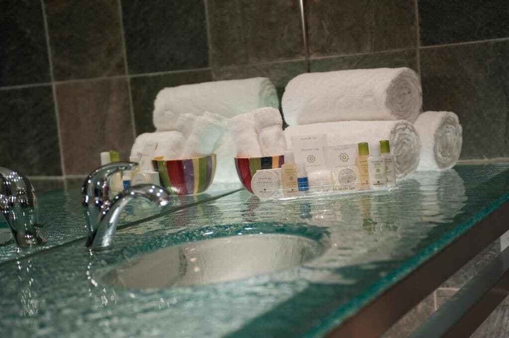 Ein Badezimmer mit einem Glaskonstruktion-Waschbecken, mehreren Handtüchern und Toilettenartikeln.