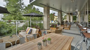 Un espacio patio al aire libre con mesas y sillas de madera, plantas en macetas y sombrillas.